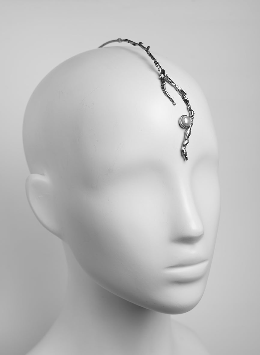 a silver piece of jewelry that adorns the head and forehead, featuring a natural pearl 