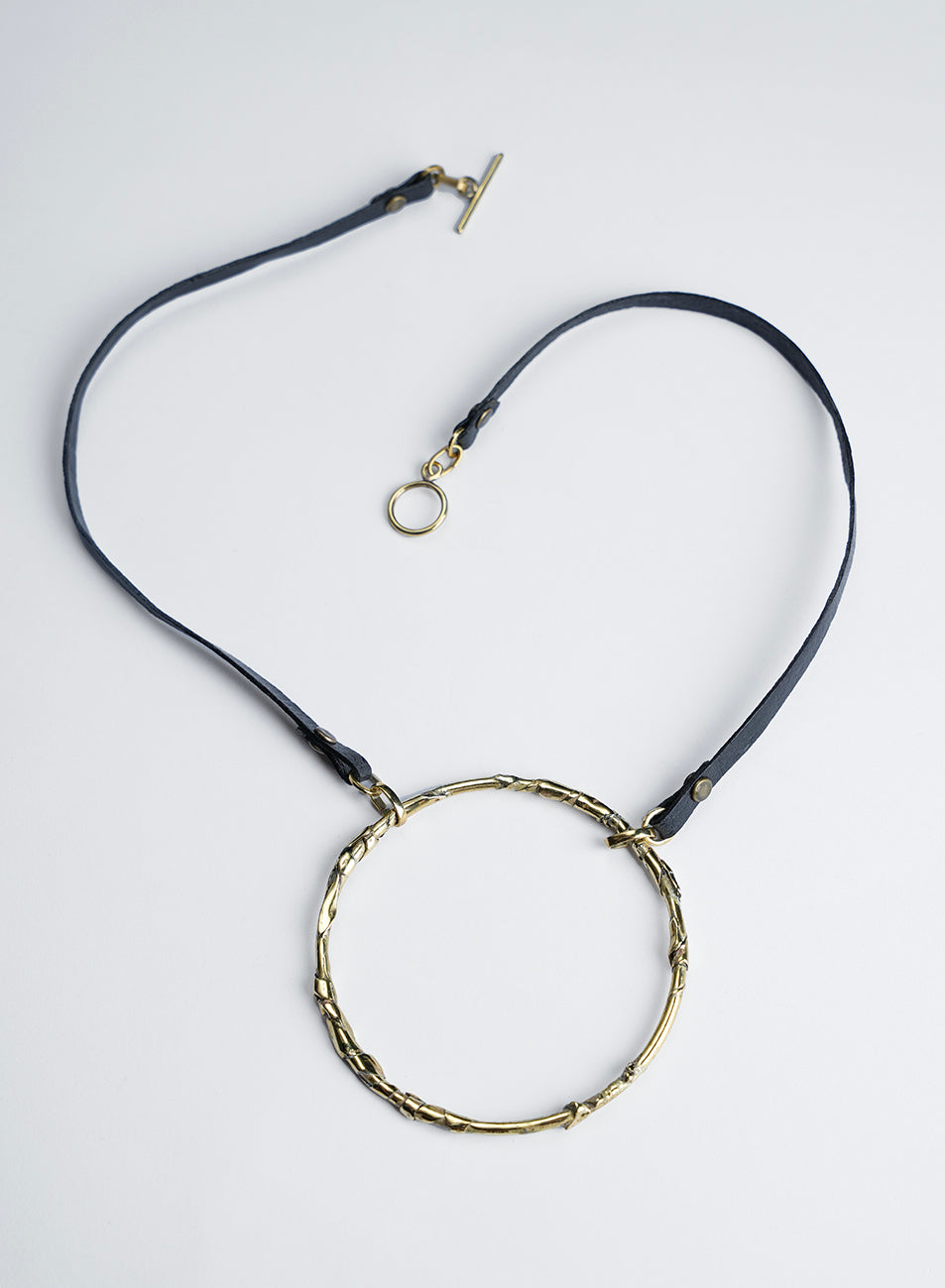 A black leather cord necklace featuring a pendant with a textured, sculpted circle; the necklace is designed to be worn short. Handcrafted. 