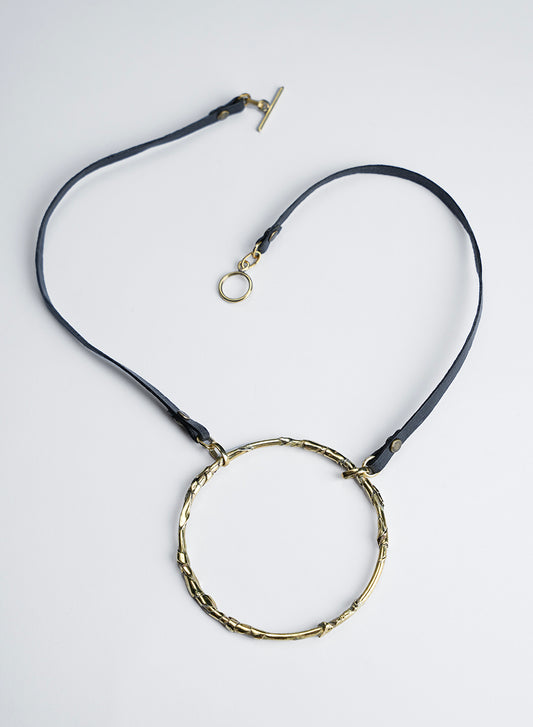 A black leather cord necklace featuring a pendant with a textured, sculpted circle; the necklace is designed to be worn short. Handcrafted. 