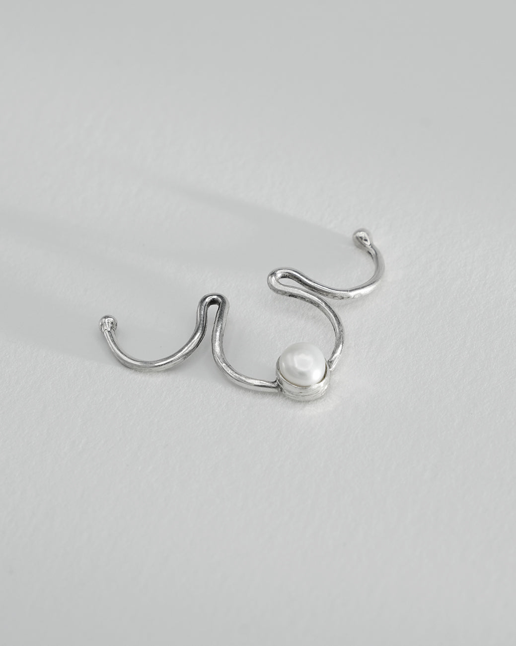 Clip-on silver septum jewelry featuring a natural pearl detail.